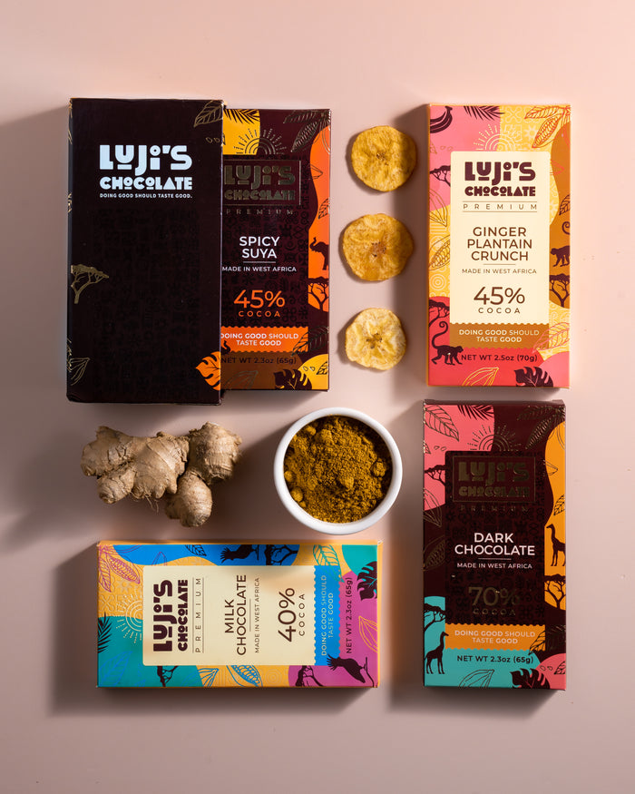 A collection of Luji's Chocolate bars displayed with their respective key ingredients, such as suya powder for the spicy suya flavor,  plantain chips for Ginger Plantain Crunch, alongside the colorful packaging of each bar.